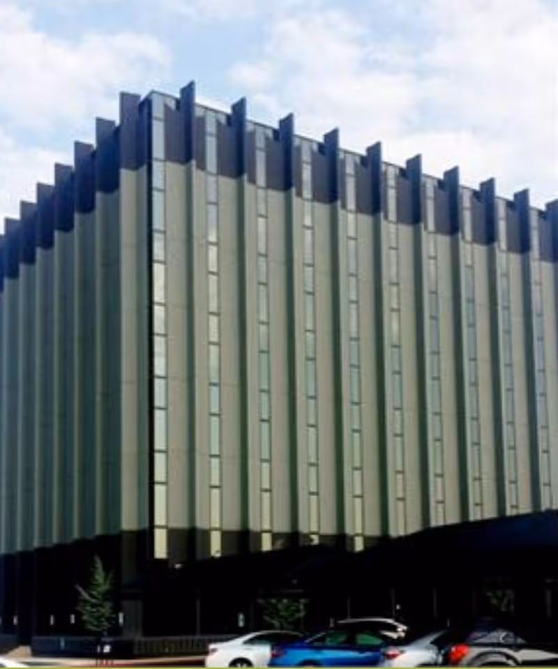 Modern multi-story building with a vertical green-gray facade and parked cars in front.