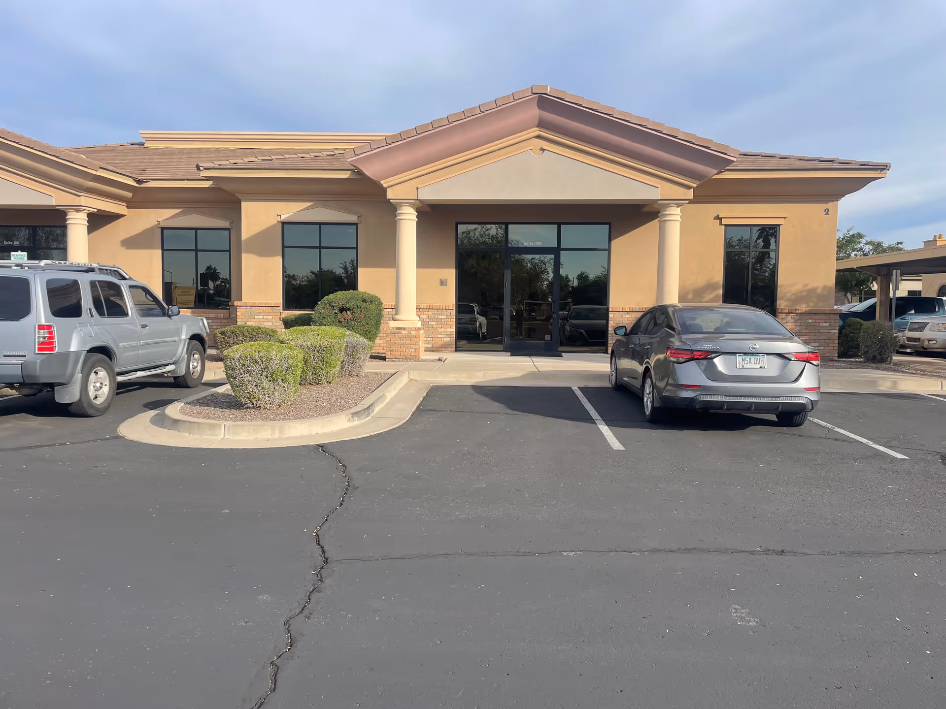 Beige senior living facility exterior with glass entrance and parked cars in front