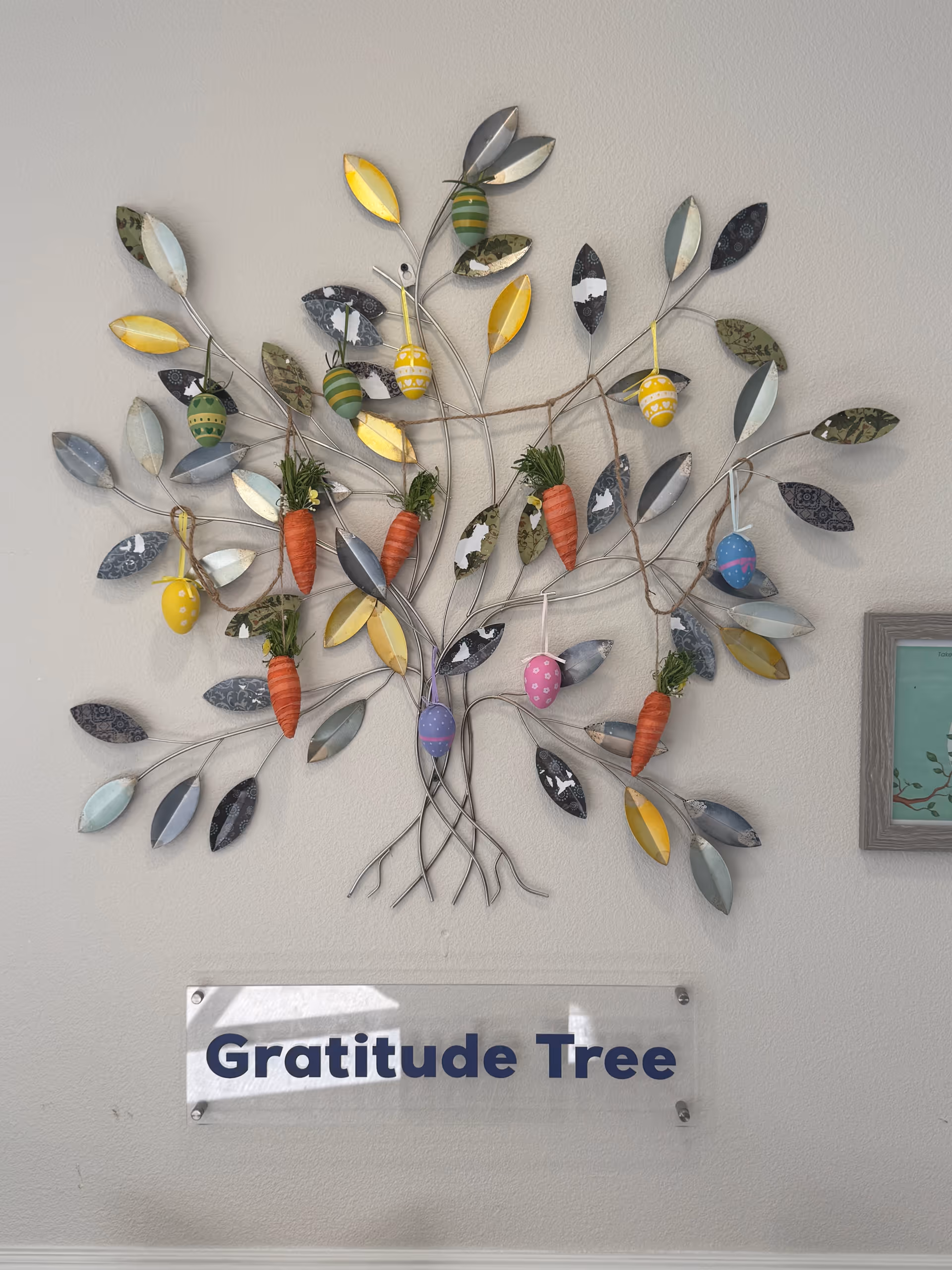 Colorful metal tree sculpture with leaves and carrots on an interior wall.