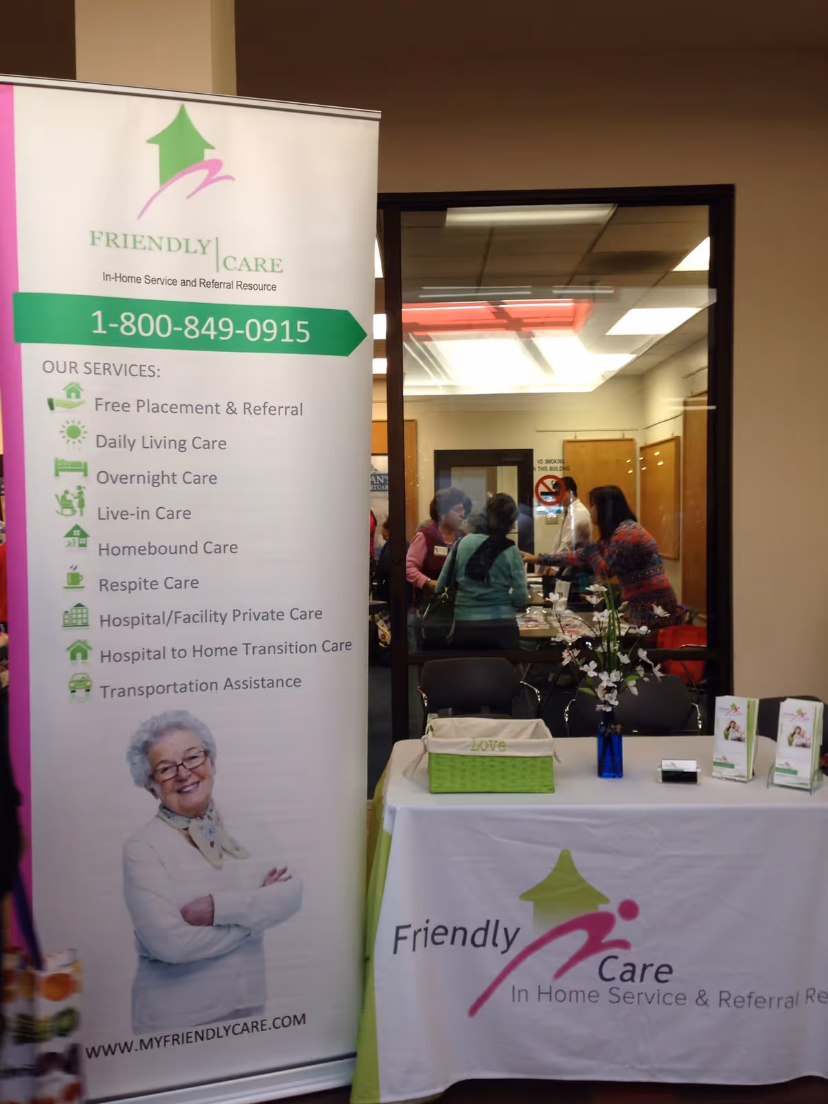 Indoor promotional display for Friendly Care with banner, reception table, and people in background