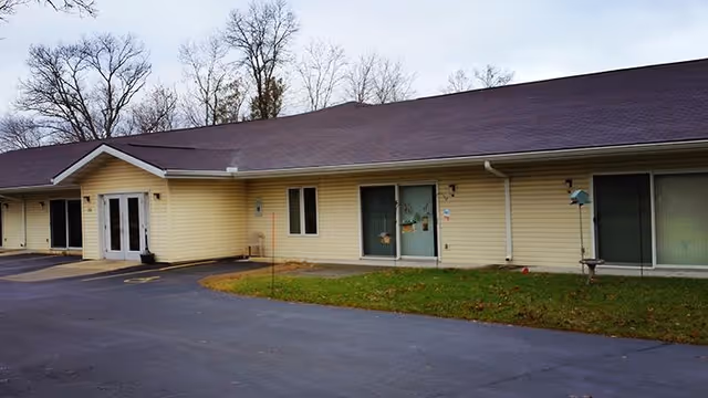 Single-story yellow siding building with sliding glass doors, a small lawn, and a paved driveway in front.