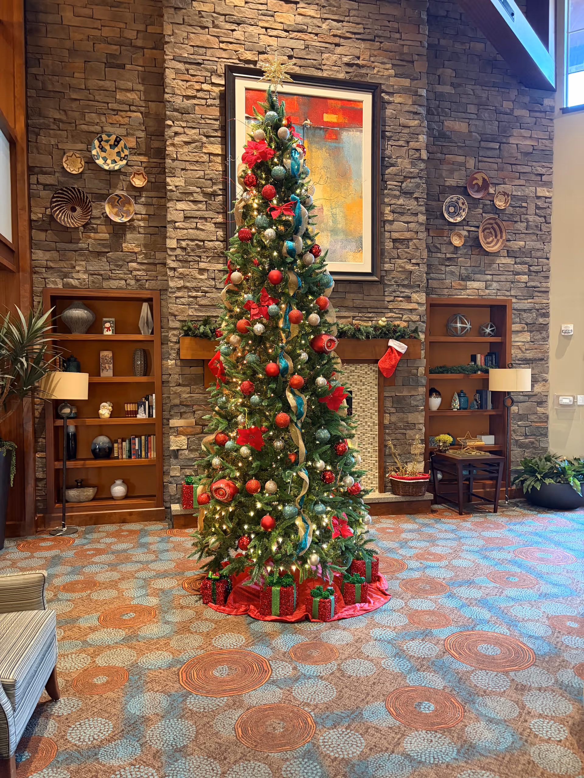 Festive Christmas tree stands in a stone-walled lobby with shelves at The Ranch Estates of Tucson.