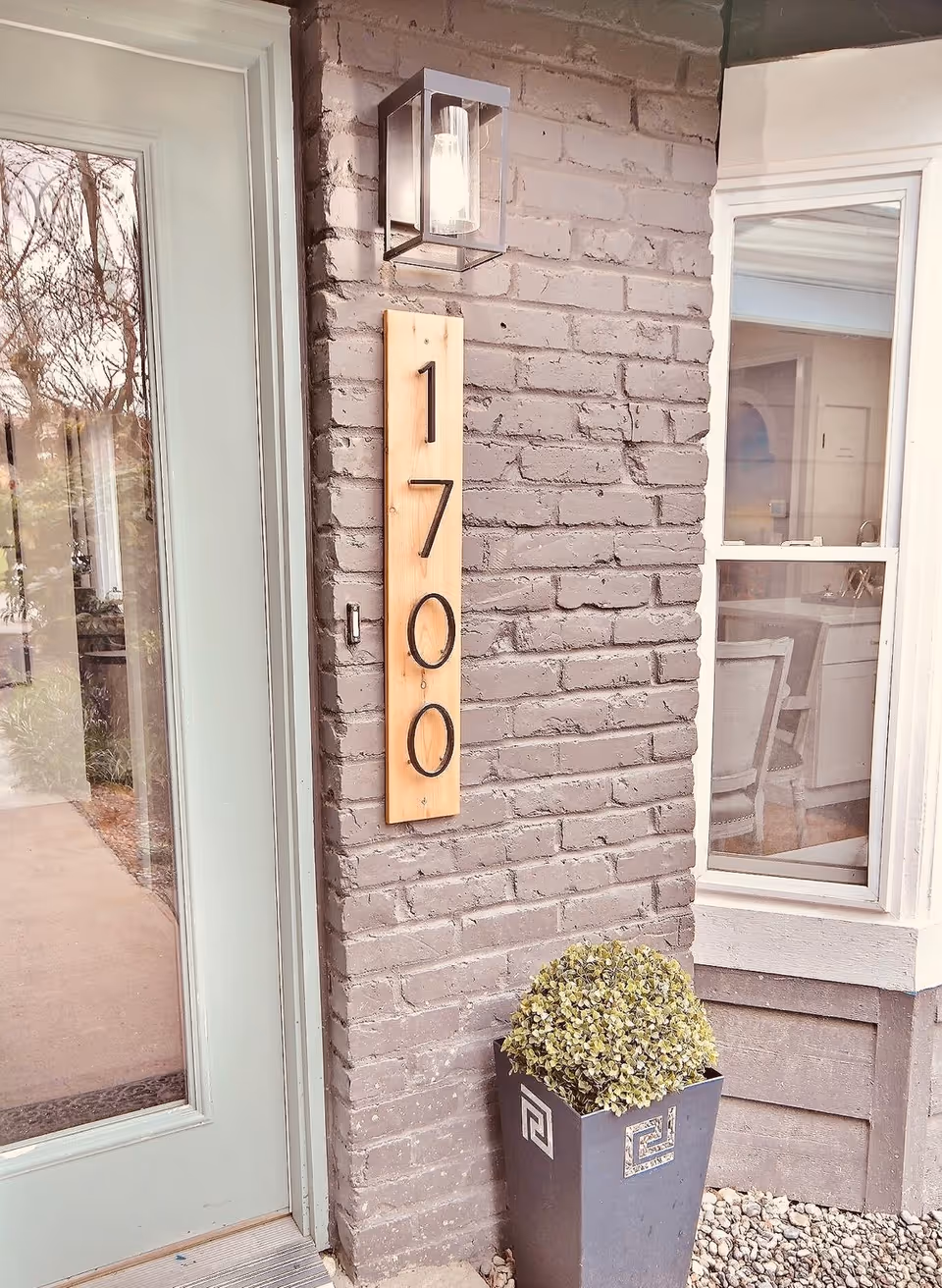 Exterior brick entrance with a vertical wooden address plaque reading 1700 and a potted plant.