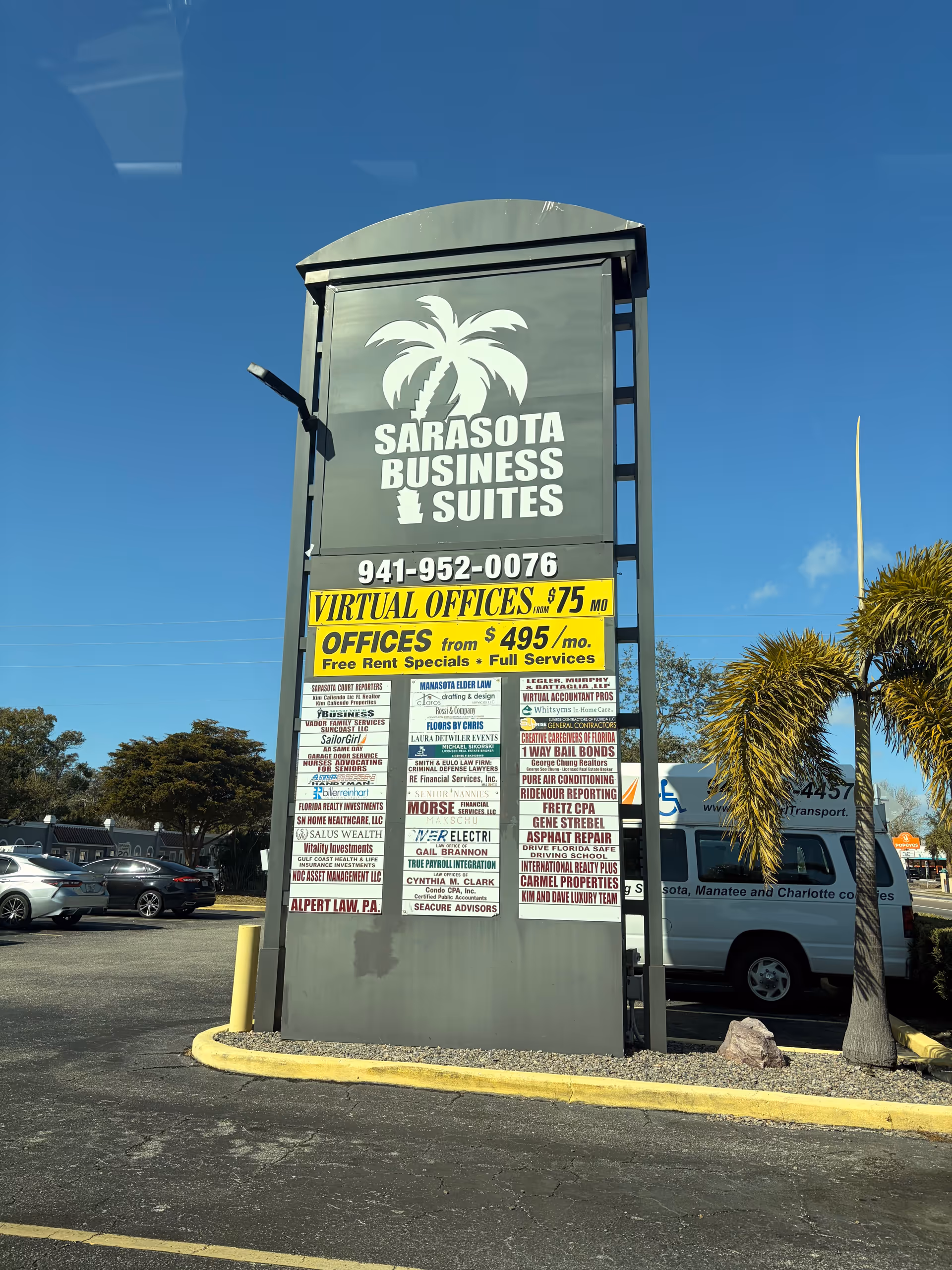 Tall outdoor sign for Sarasota Business Suites with banners and parked cars nearby.