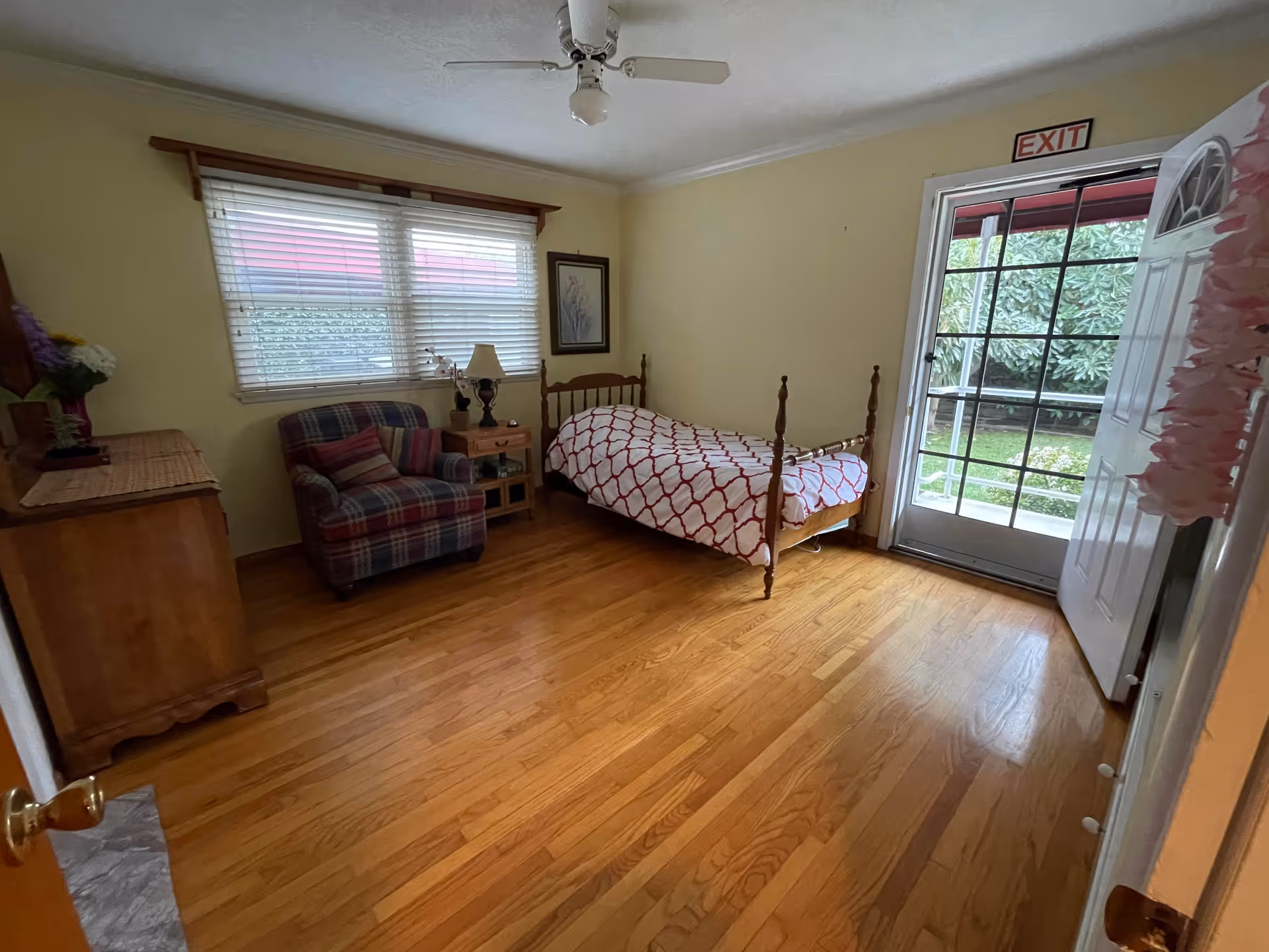 Bedroom in Violet Residential Care with a four-poster bed, dresser, chair, and exit door.