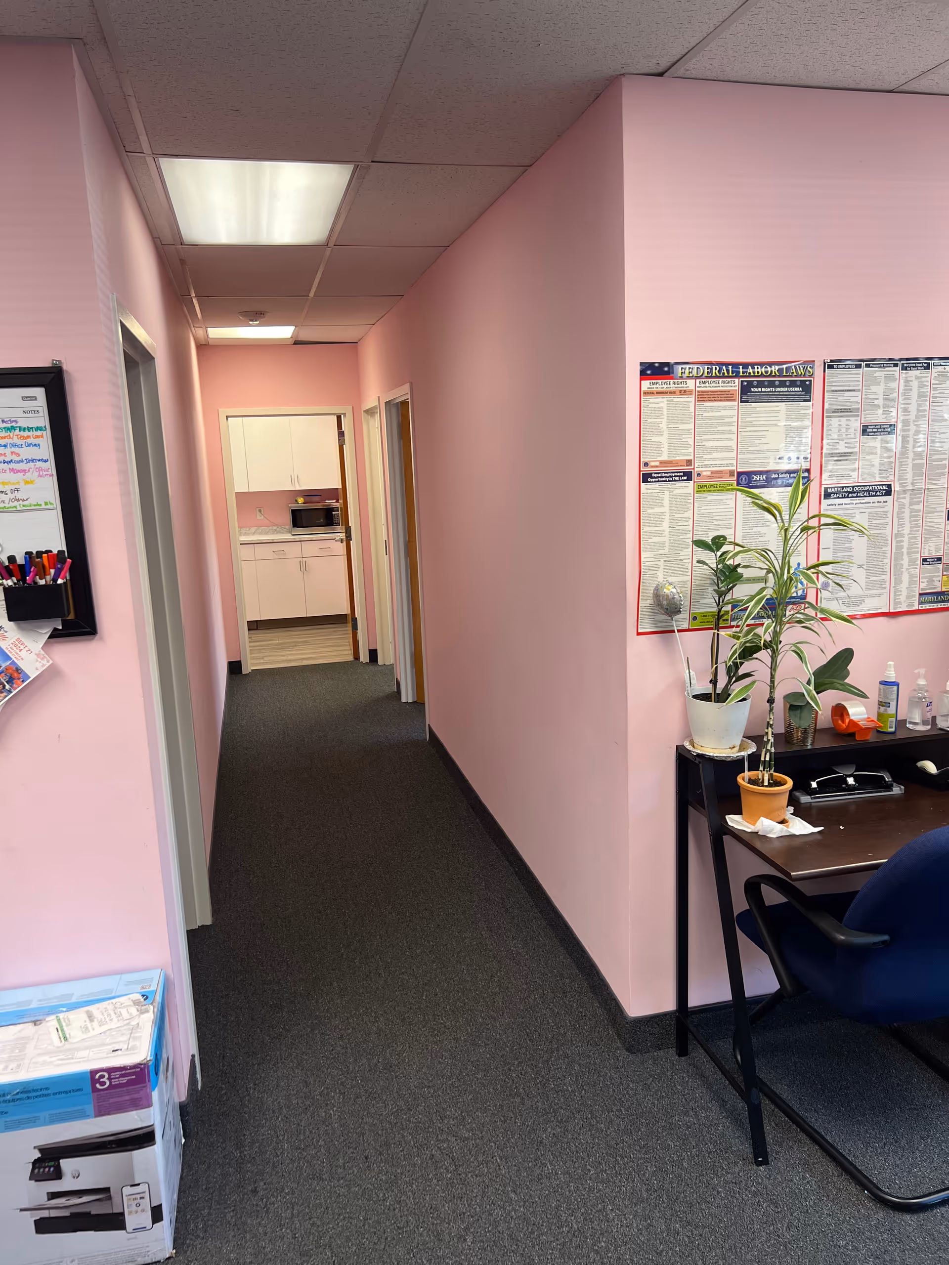 Pink-walled interior hallway of a senior living facility with desk and plants.