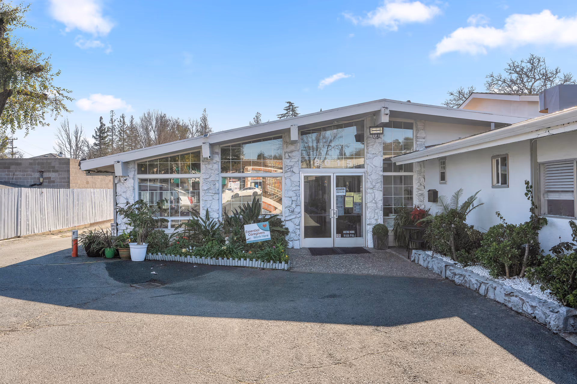 Front entrance of the Walnut Creek Willows building with large glass windows, potted plants, and a driveway.