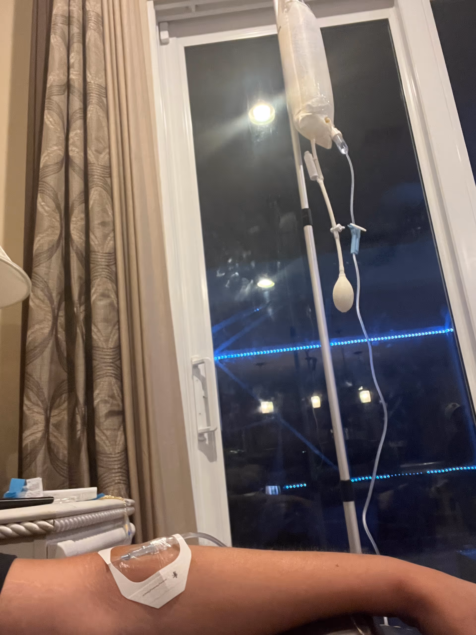 Hospital room with IV pole, IV bag, and patient arm in foreground.