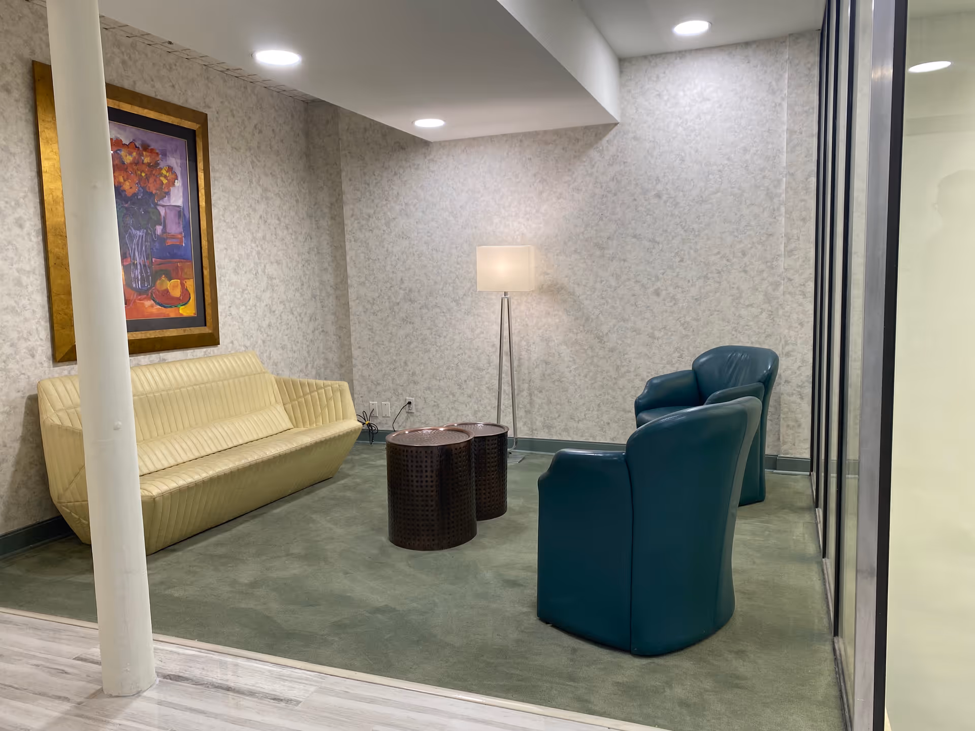 A modern facility lounge with cream sofa, teal chairs, tables, lamp, and artwork.