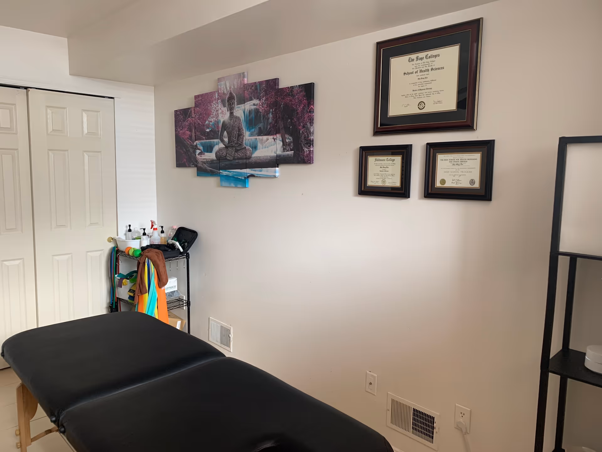 Massage therapy table in a small room with wall certificates and a rolling cart.