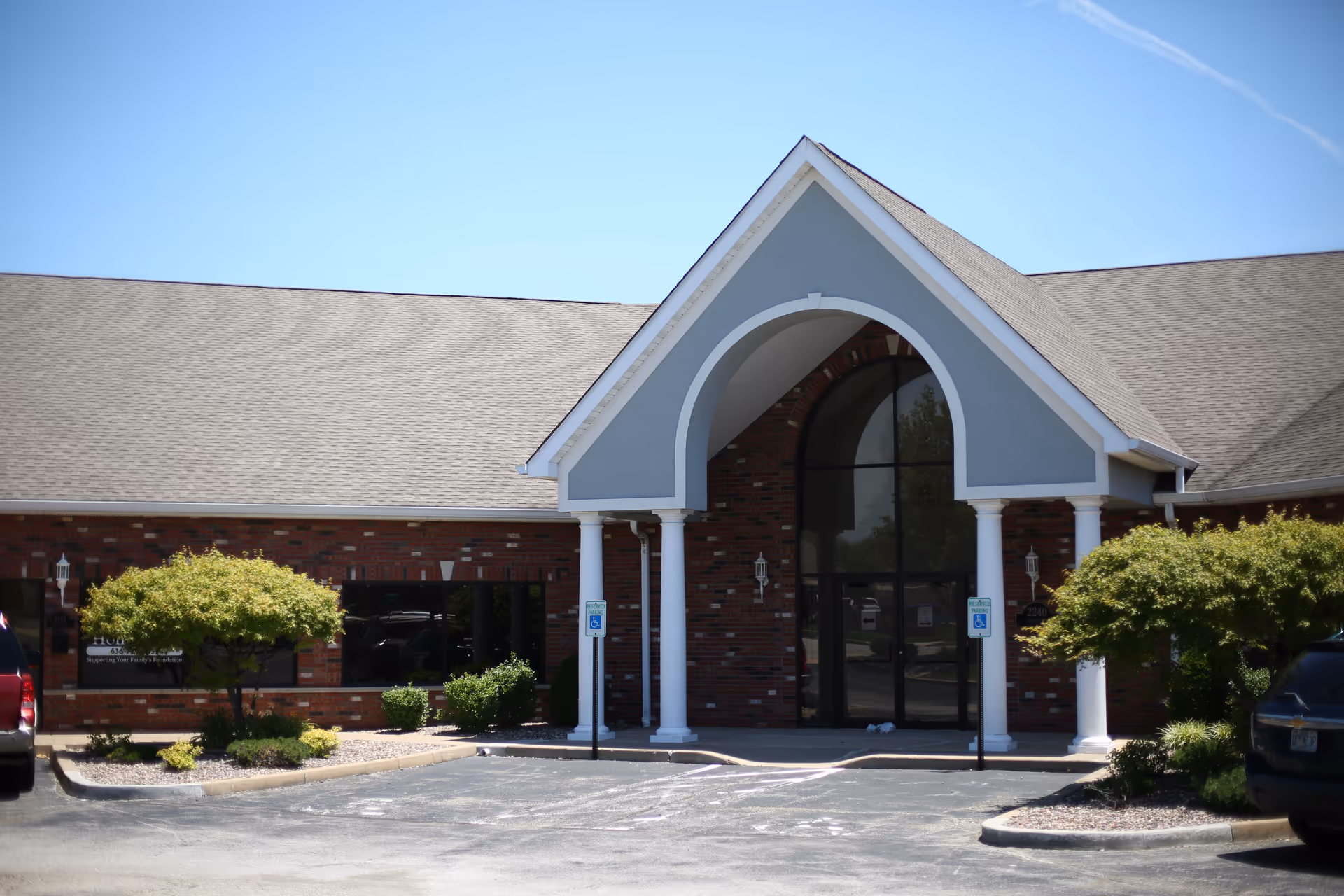Brick senior living facility with arched entrance and white columns.