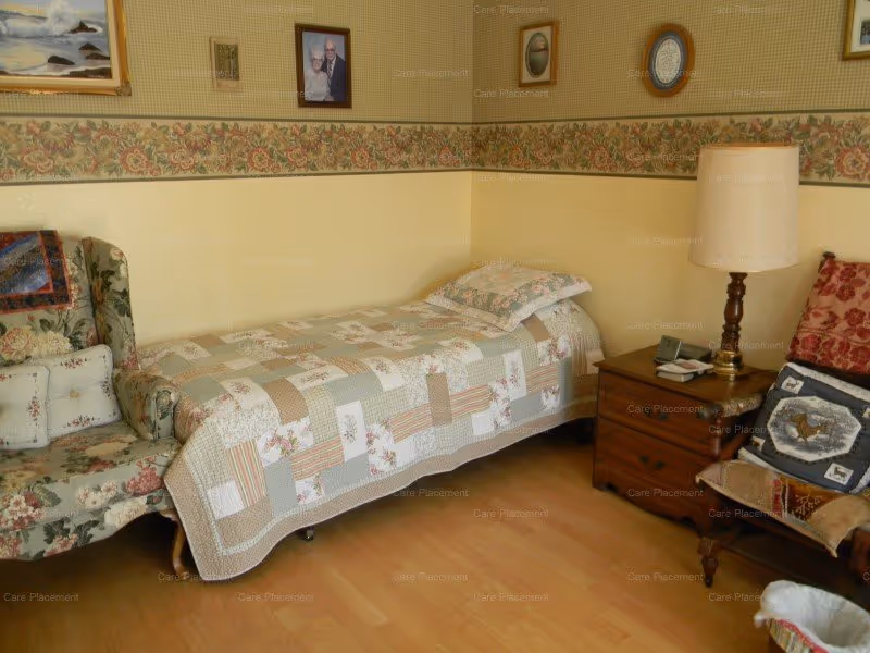 A cozy Mary Katherine's Cottage bedroom with a quilted bed, nightstand, lamp, and seating.