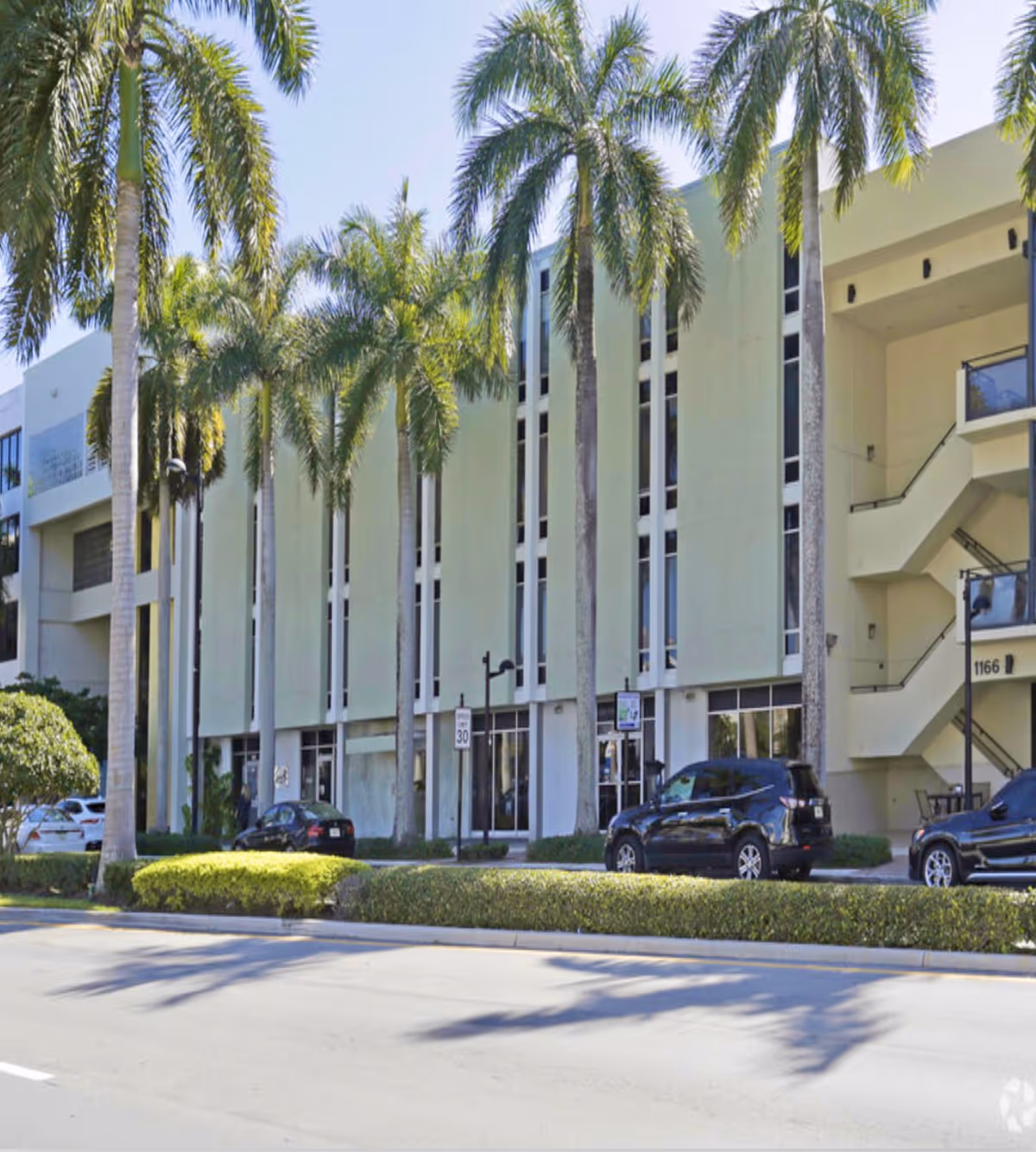 Exterior view of a multi-story senior living building with palm trees and parked cars.