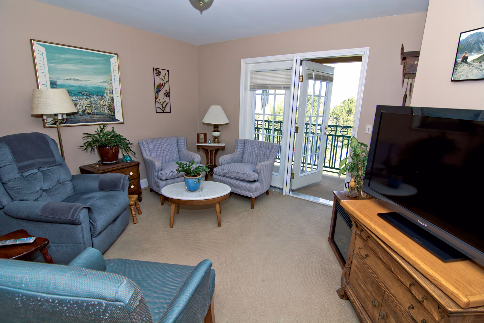 A cozy living room with blue chairs, a round coffee table, and a balcony door.