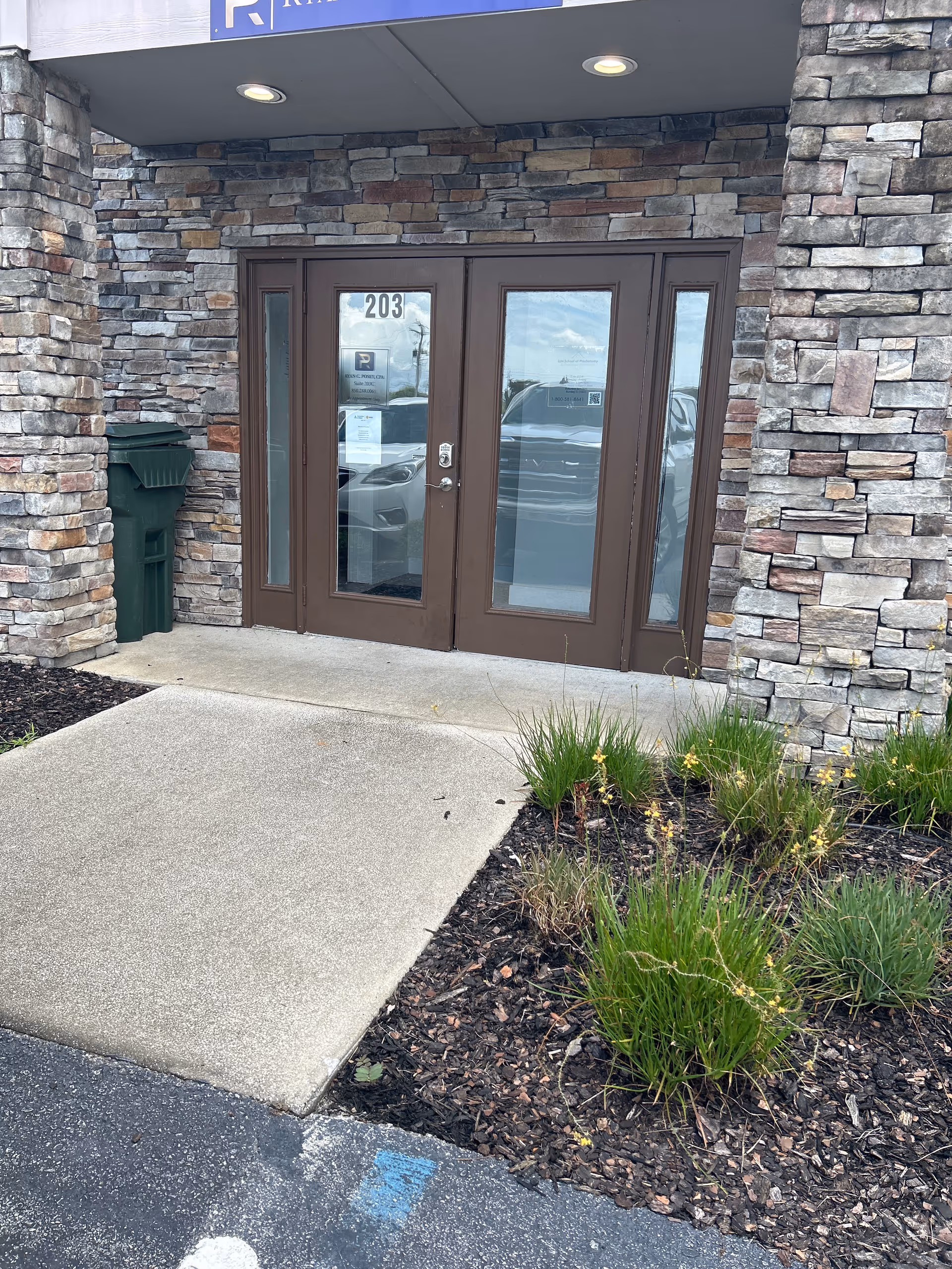 Stone-clad building entrance with glass doors, landscaping, and the number 203.