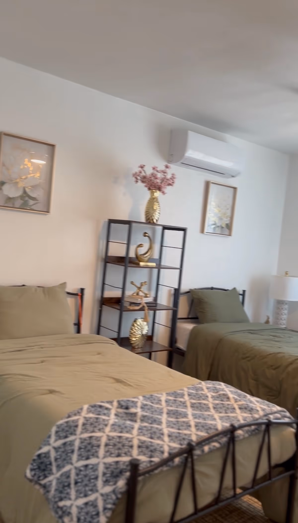 Two single beds with green comforters and a decorative shelf between them in a bedroom.