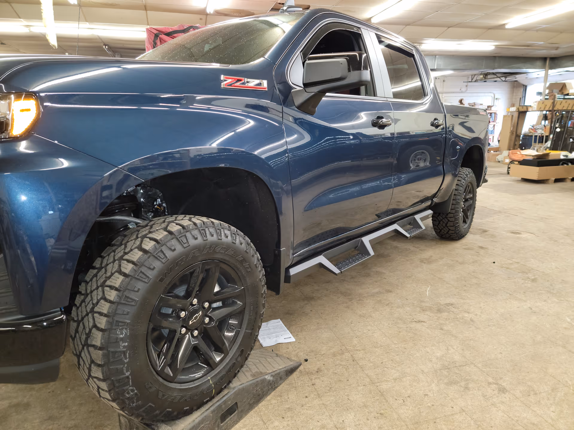 Blue pickup truck lifted on a service hoist inside a workshop