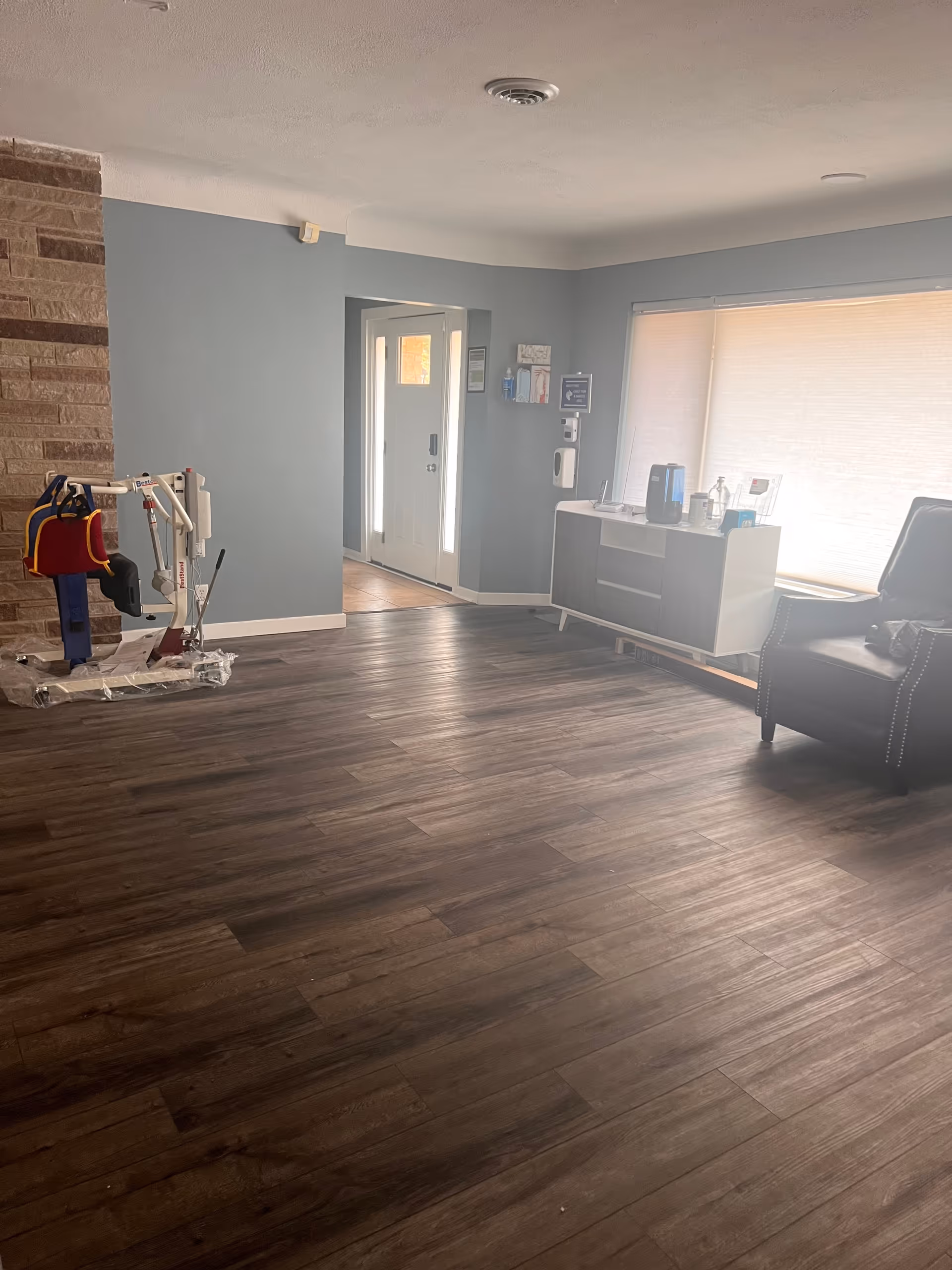 Interior living area with a dark sofa, cabinet, window blinds, and a mobility lift device.