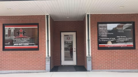 Brick building entrance with glass door and signs for Caring Friends In-Home Care.