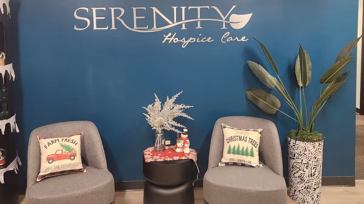 Two gray chairs sit in front of a blue wall with Serenity Hospice Care signage.