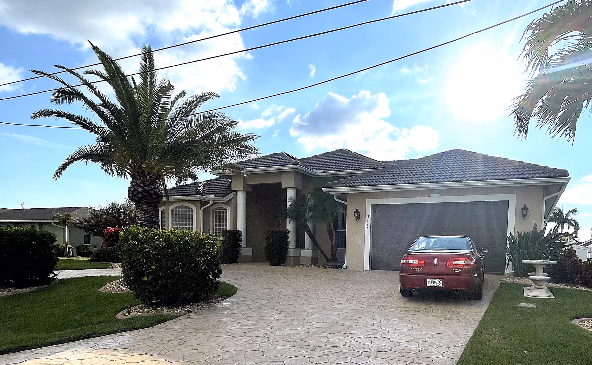 Single story suburban house with a driveway, palm trees, and a parked red car.
