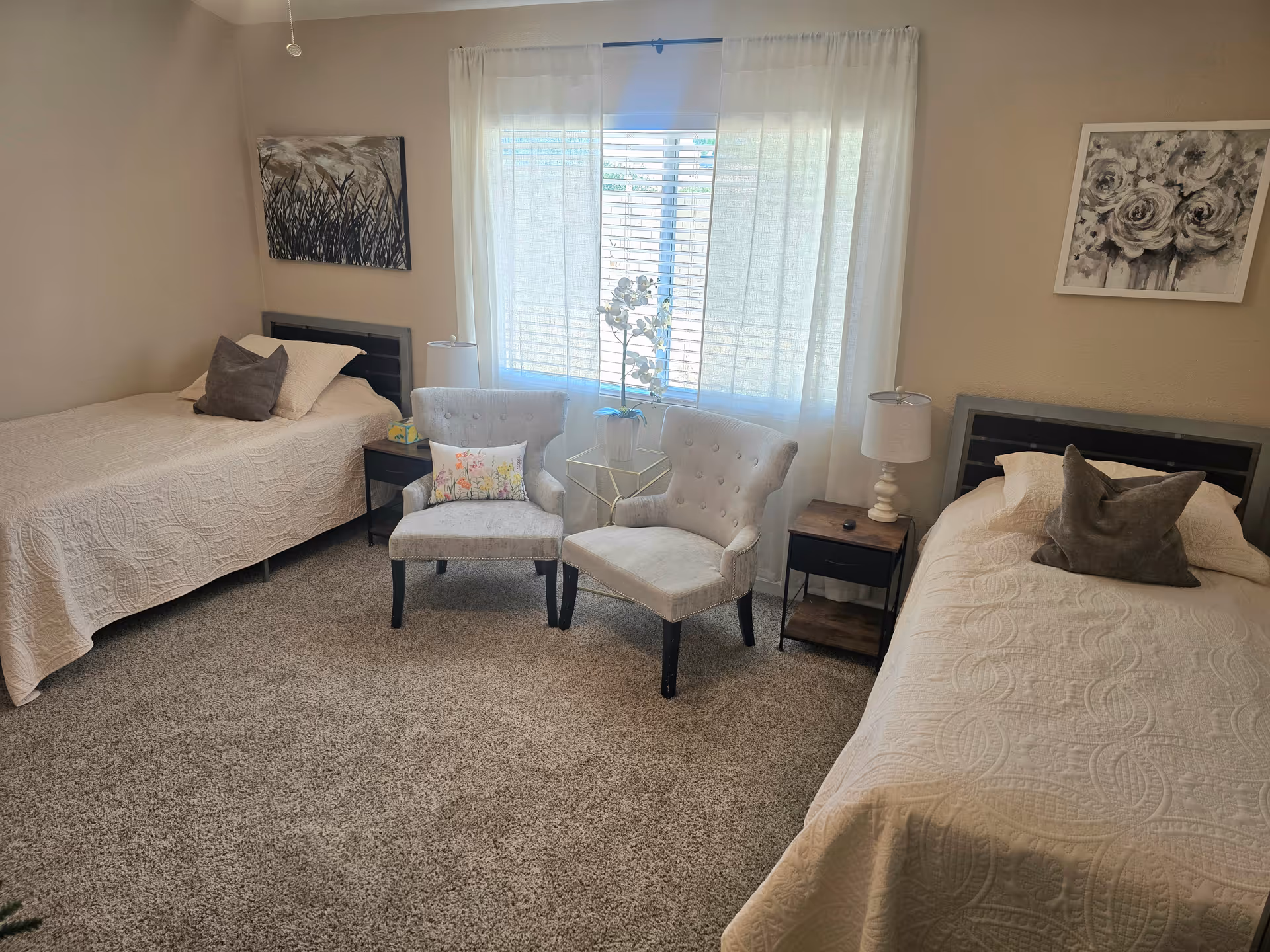 A cozy bedroom with two twin beds, two chairs, nightstands, and sheer curtains.