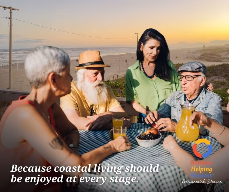 Group of seniors sits around a table outdoors by the beach at sunset.