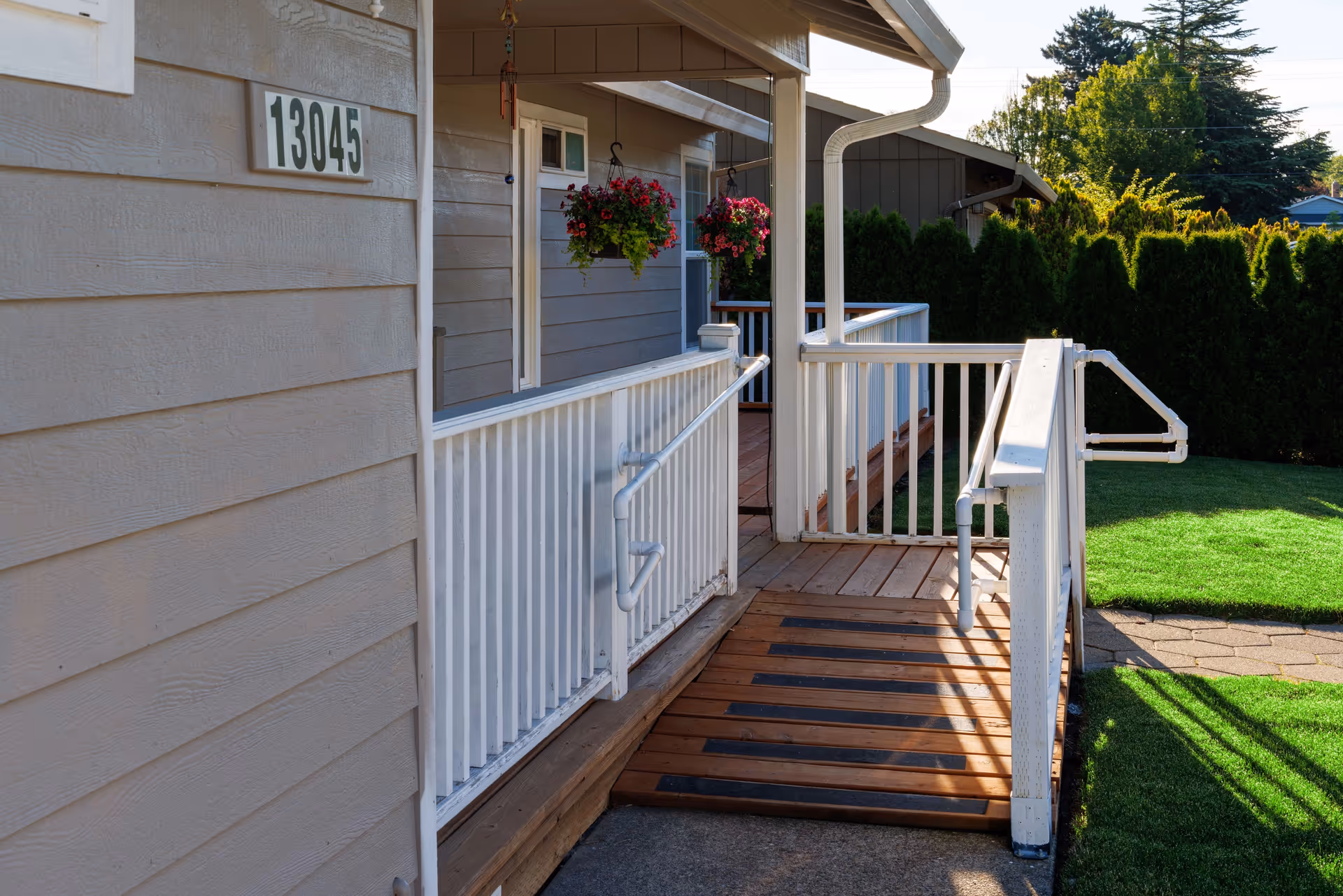 Exterior view of Tunai Adult Care Home with ramp, white railings, hanging baskets, and lawn