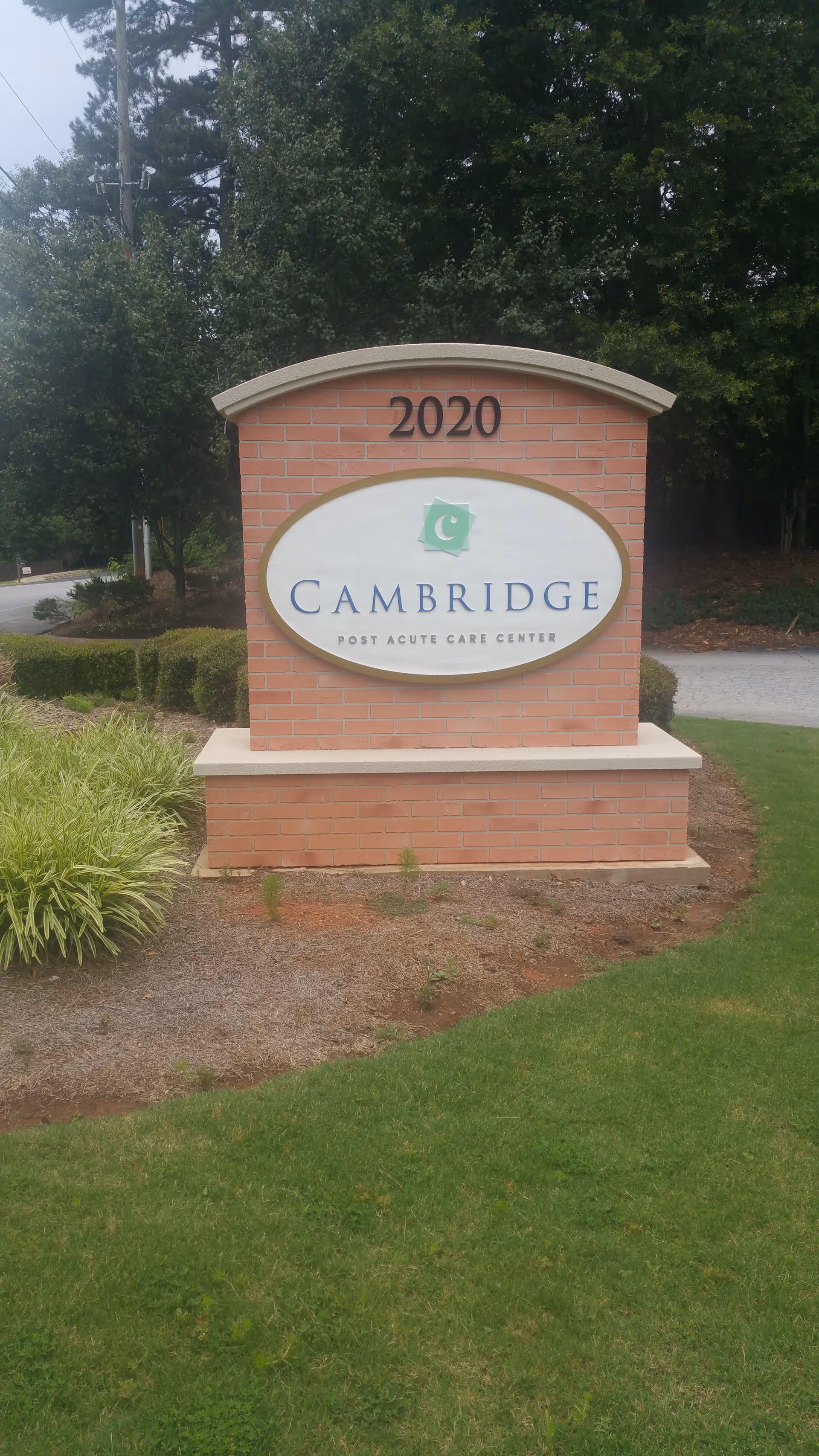 Brick entrance sign reading Cambridge Post Acute Care Center with 2020 atop, surrounded by landscaping.