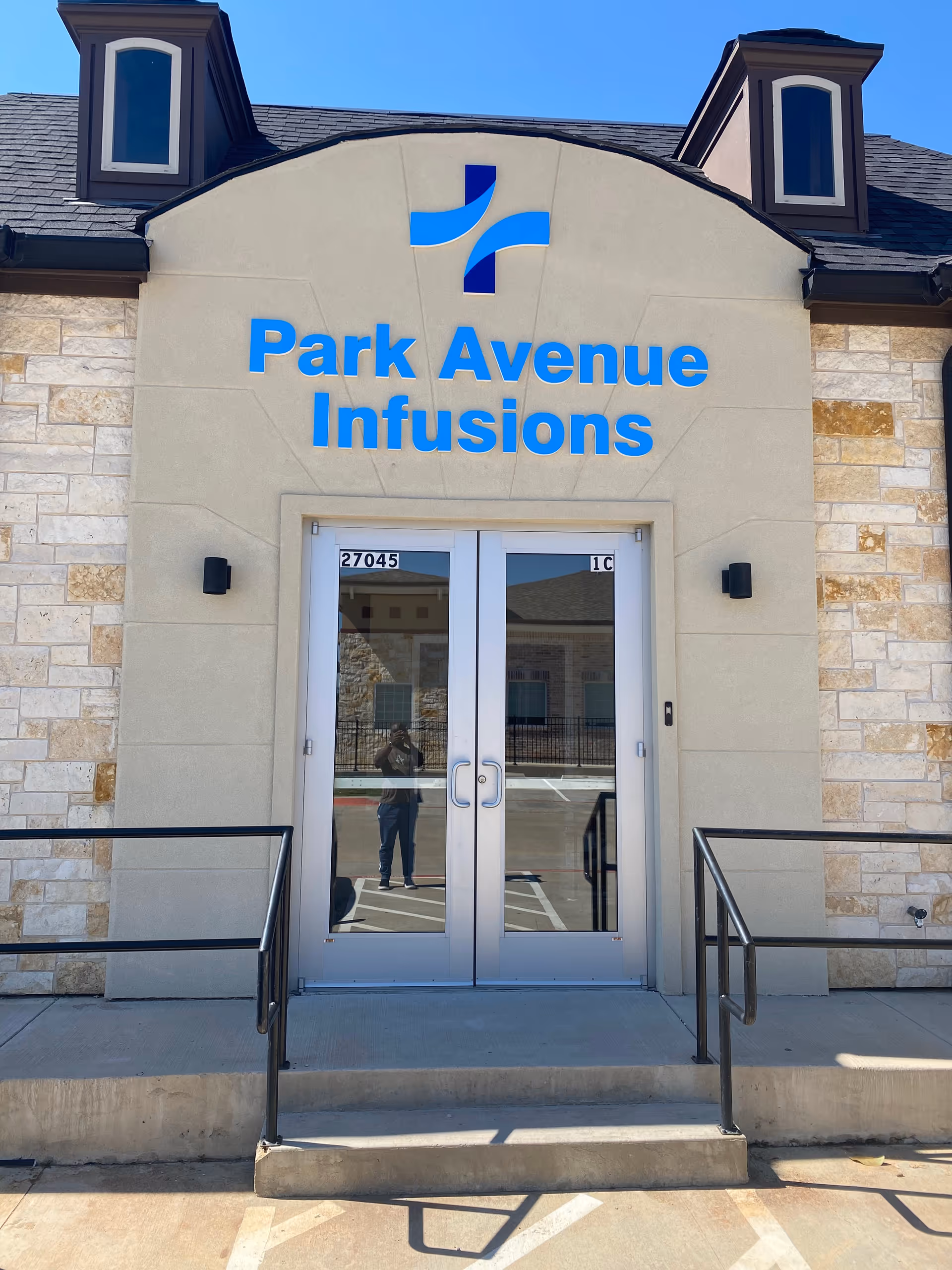 Front entrance of Park Avenue Infusions with double glass doors and blue sign on stone facade.