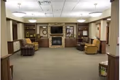 Spacious living room lounge in a senior facility with seating, built-ins, and a central fireplace.