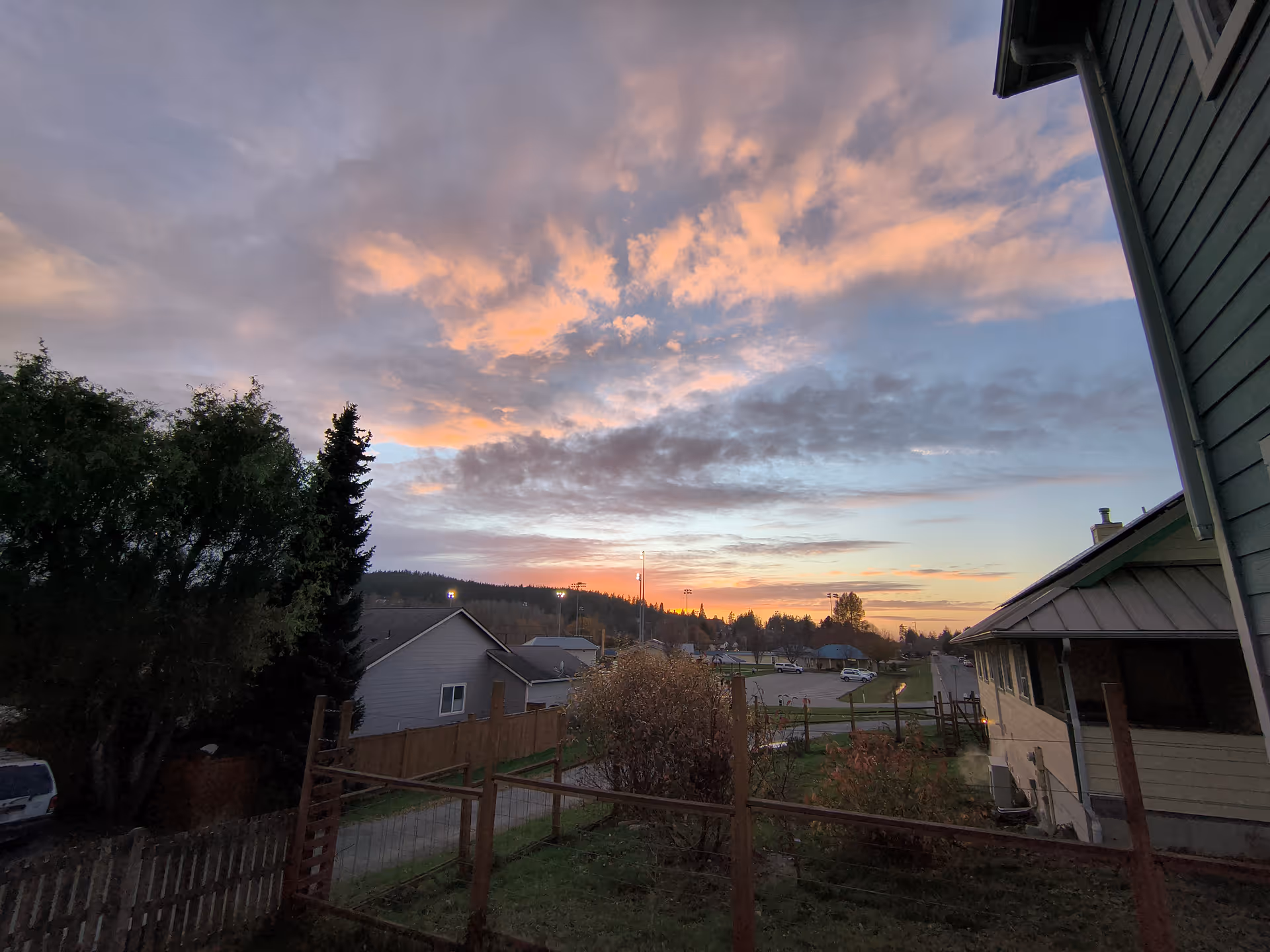 Sunset over a residential outdoor scene with fences, trees, and neighboring houses beside the retirement building.