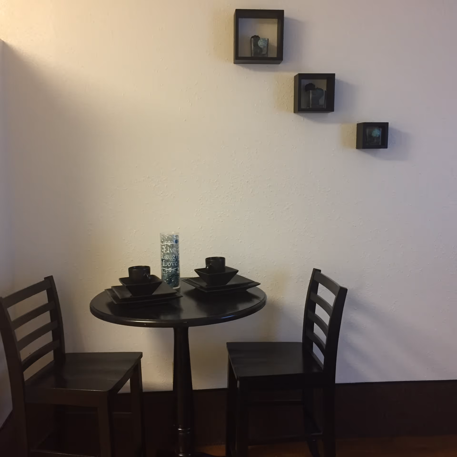 Small round black table with two chairs and wall-mounted decorative boxes.