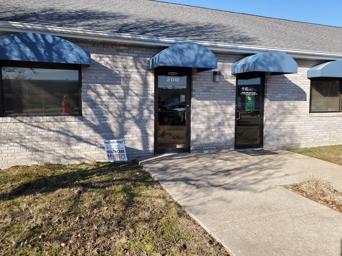 Brick facility entrance with two glass doors and blue curved awnings.