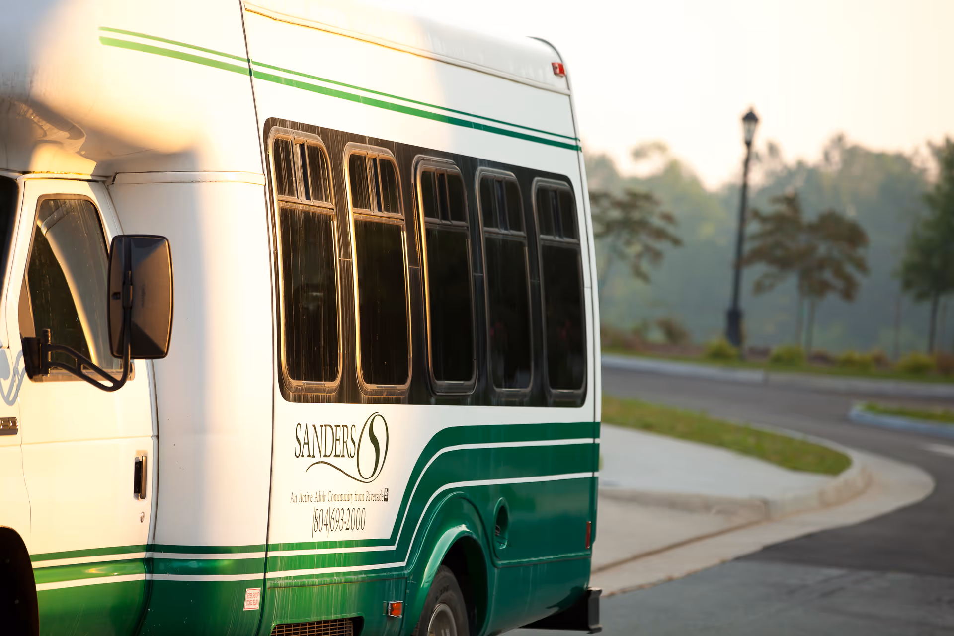 White and green Sanders Assisted Living Residence shuttle bus parked beside a curved road.