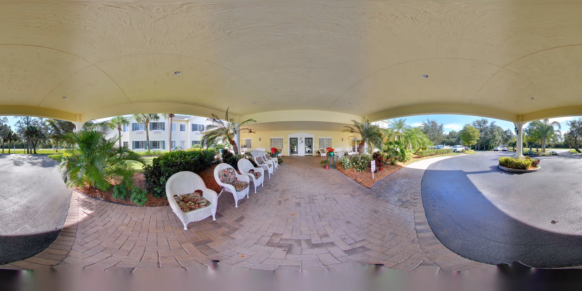 Covered porte-cochère entrance at Lexington Manor with a row of wicker chairs, potted plants, and the building facade beyond.