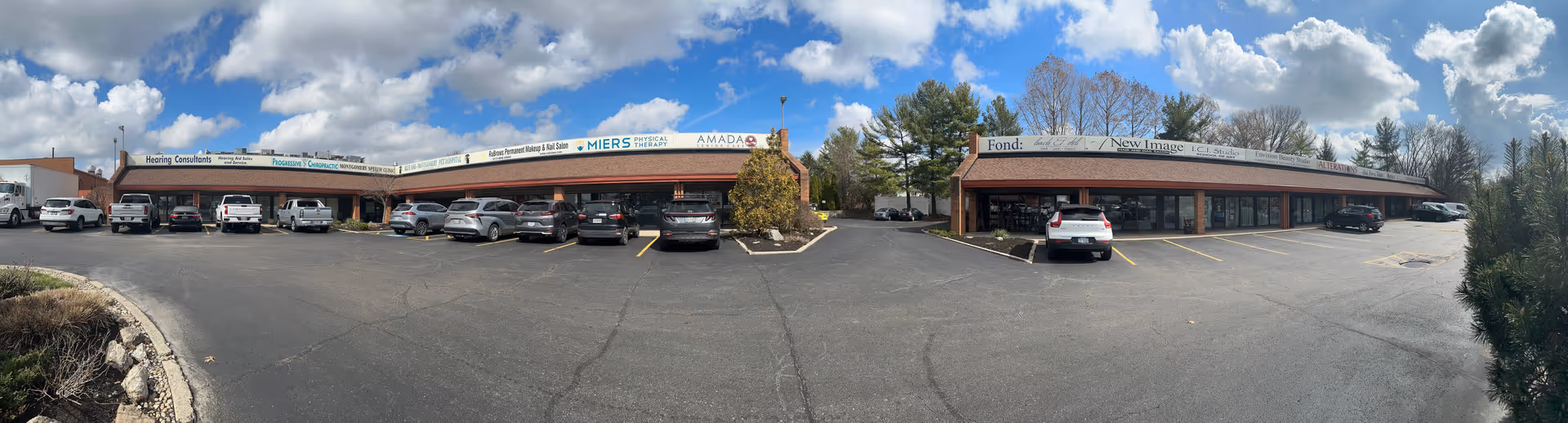 Panoramic view of a strip plaza with Amada Senior Care storefront and parking.