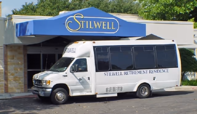 Exterior view of Stilwell Retirement Residence entrance with a white bus under a blue canopy.