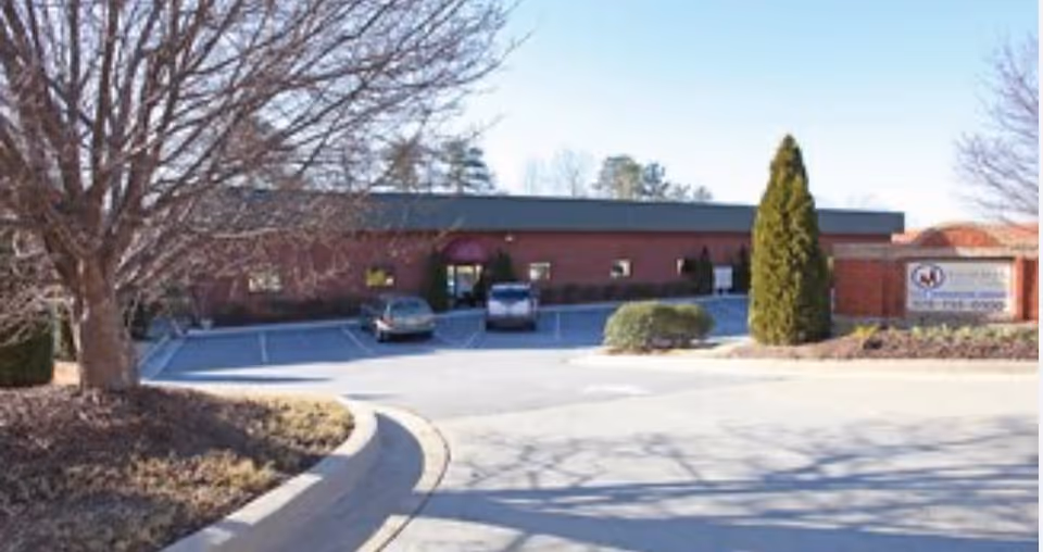 Front exterior of a brick senior care facility with parking and a sign.