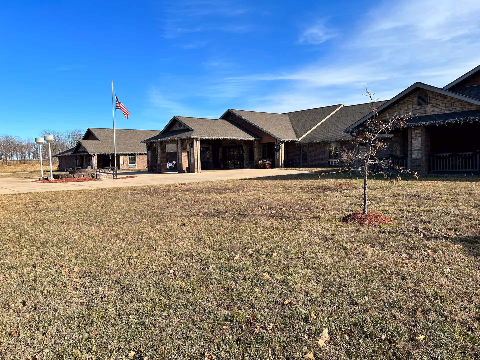 Front view of a brick Country Living Assisted Living building with a flagpole and blue sky.