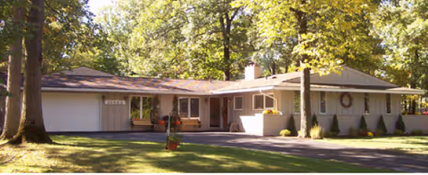 Single-story building with a wide front entrance, surrounded by trees and a manicured lawn.