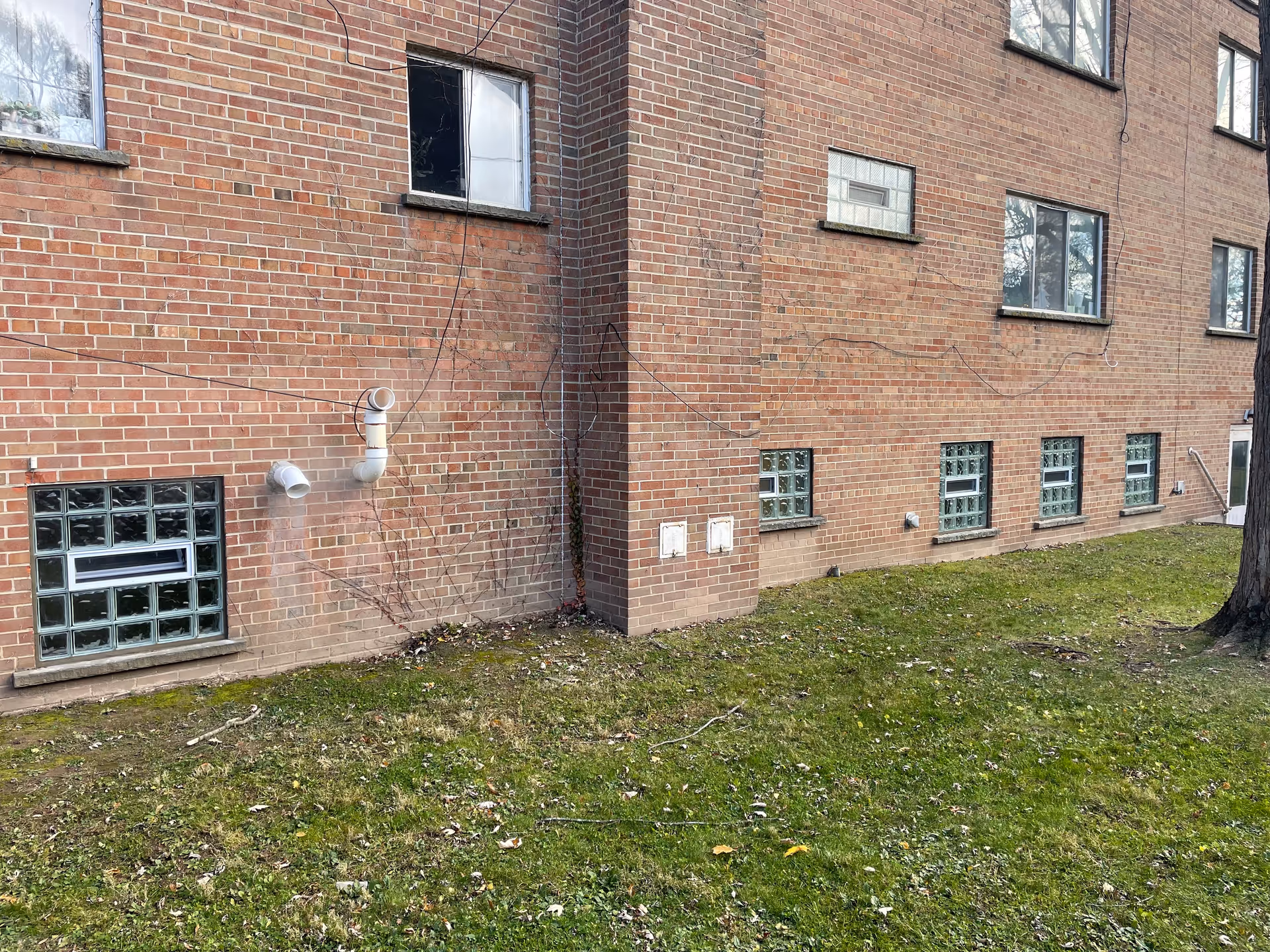 Brick exterior of a senior living facility with pipes, vents, windows, and a grassy area.