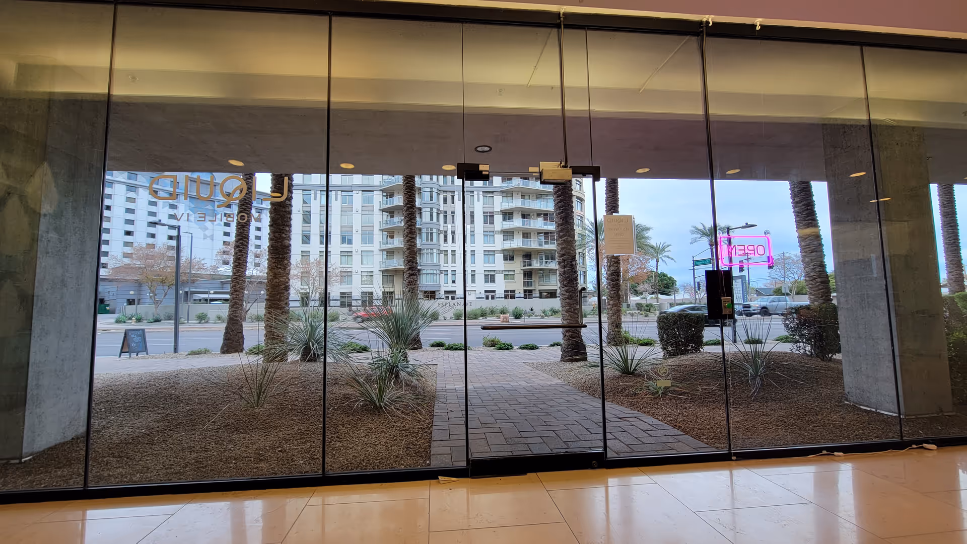 Glassy building entrance with palm trees and a courtyard visible through large windows.