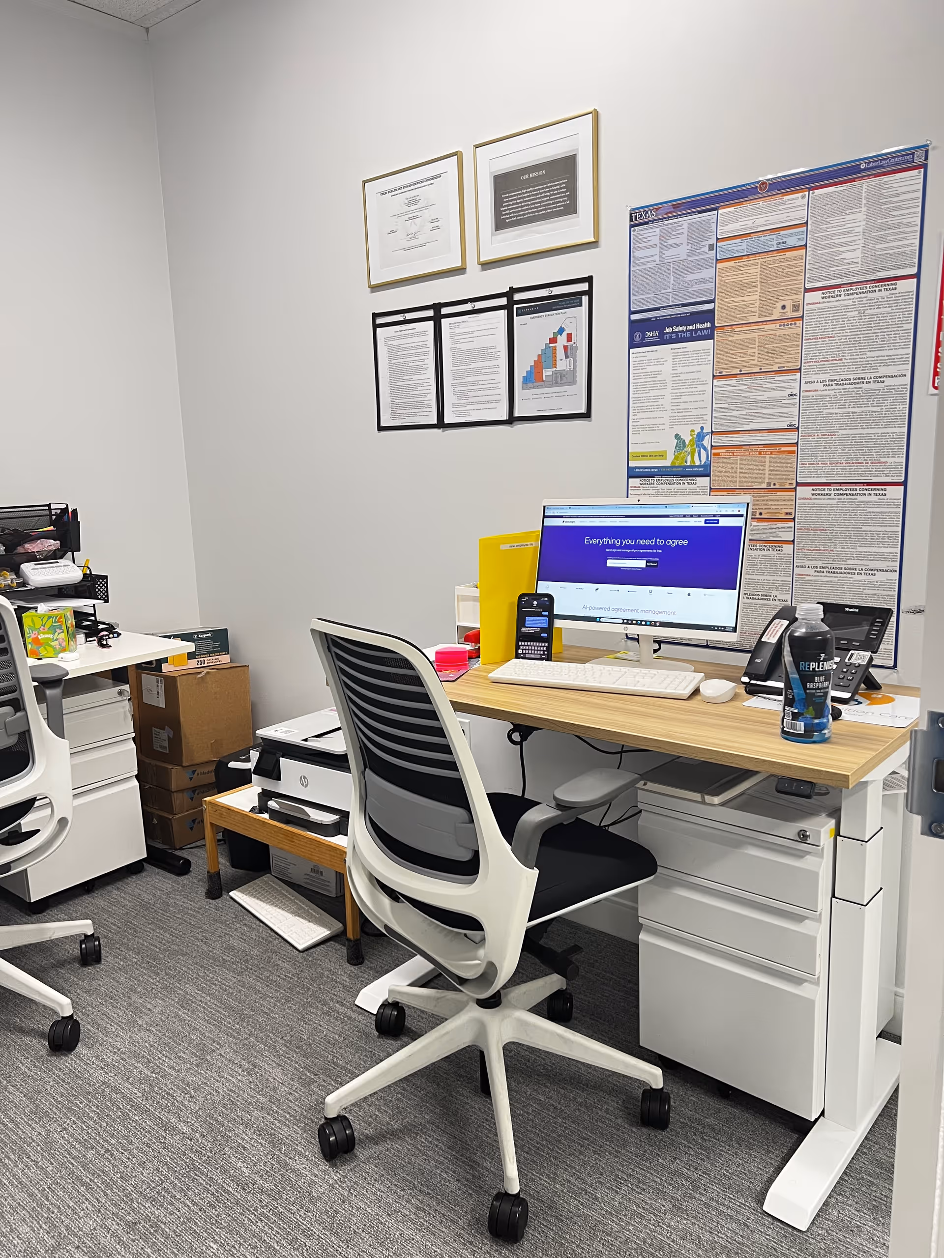 Office workspace with computer desk, chair, printer, and wall posters.