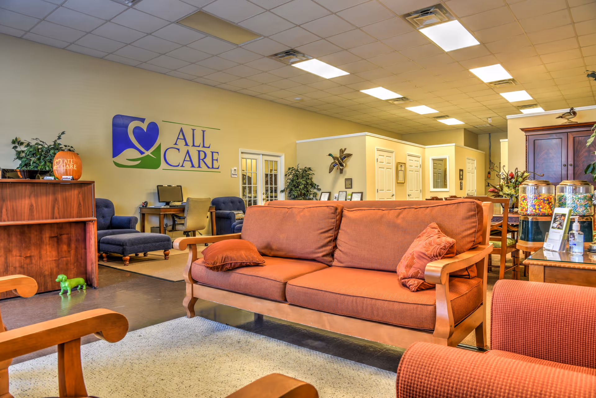 Lobby seating area with orange couches and an All Care sign on the wall.