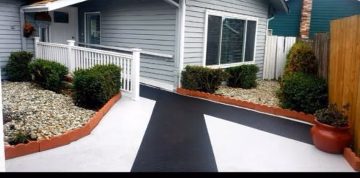 Front of a grey house with a black-and-white walkway and landscaped beds.
