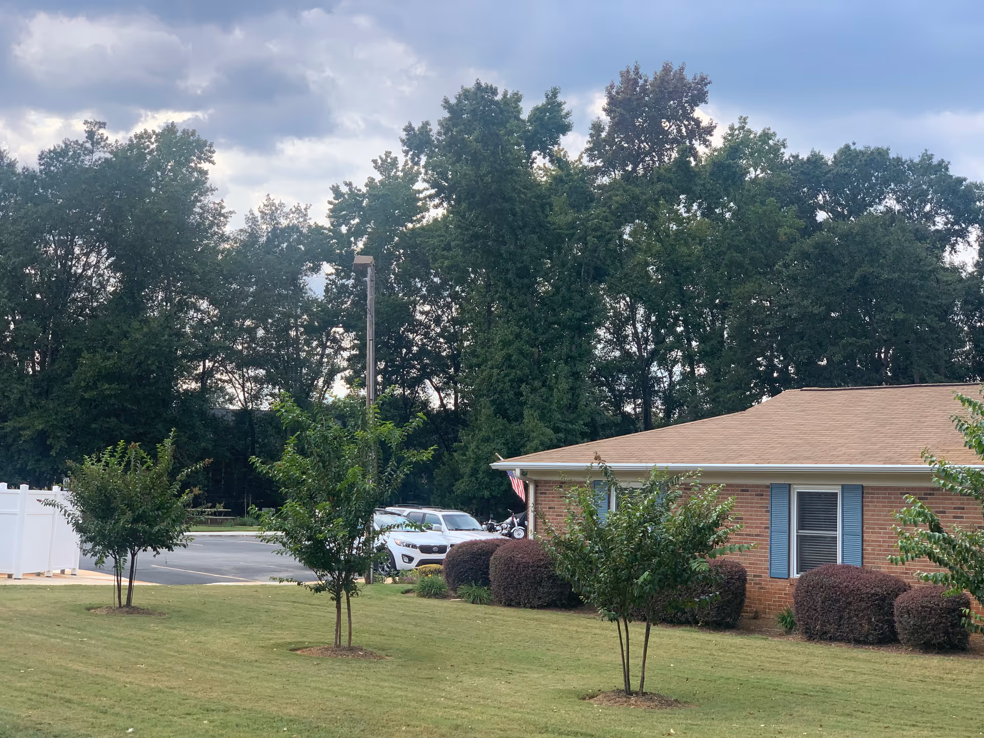 Exterior view of Miller Oaks Westminster Community showing a brick building, shrubs, trees, and parking lot.