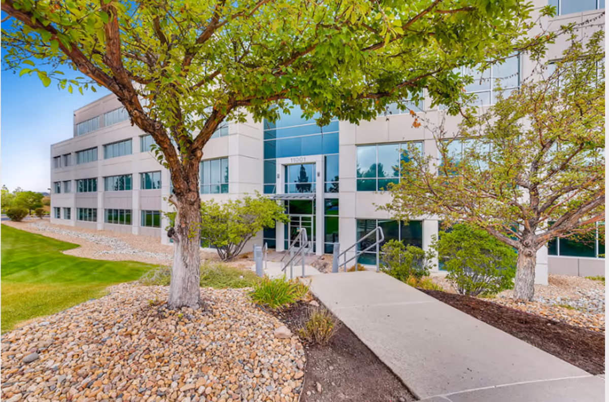 Modern senior living facility exterior with glass entry, concrete ramp, and landscaped rocks.