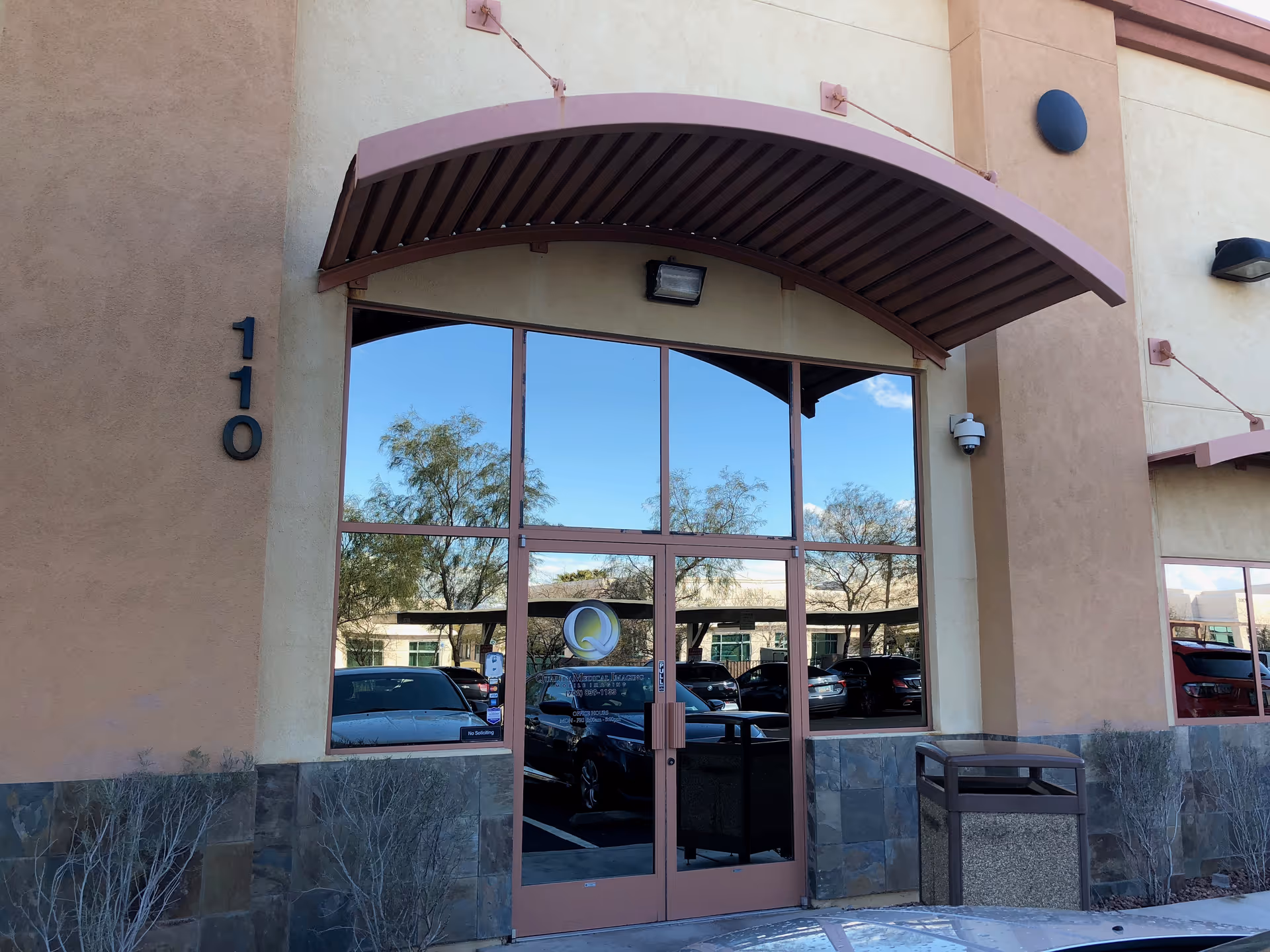 Front entrance of a beige building with glass doors and a curved brown awning.