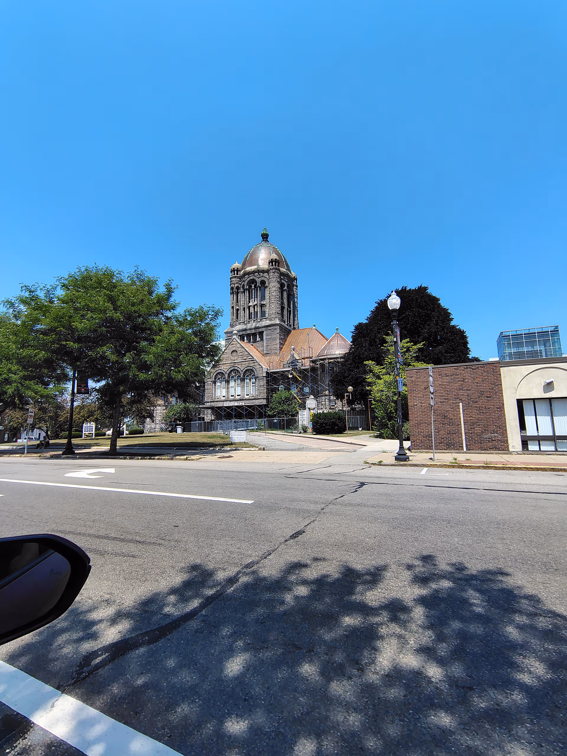Street view of a domed historic building with trees, road, and blue sky.